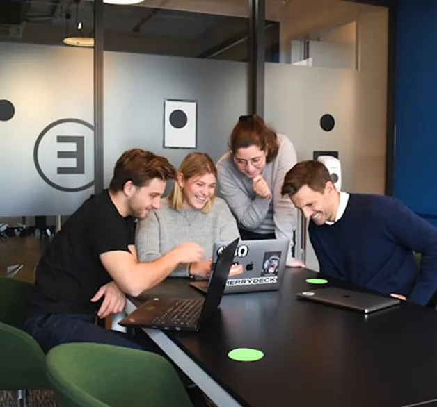 Four colleagues smiling and looking at a laptop together.