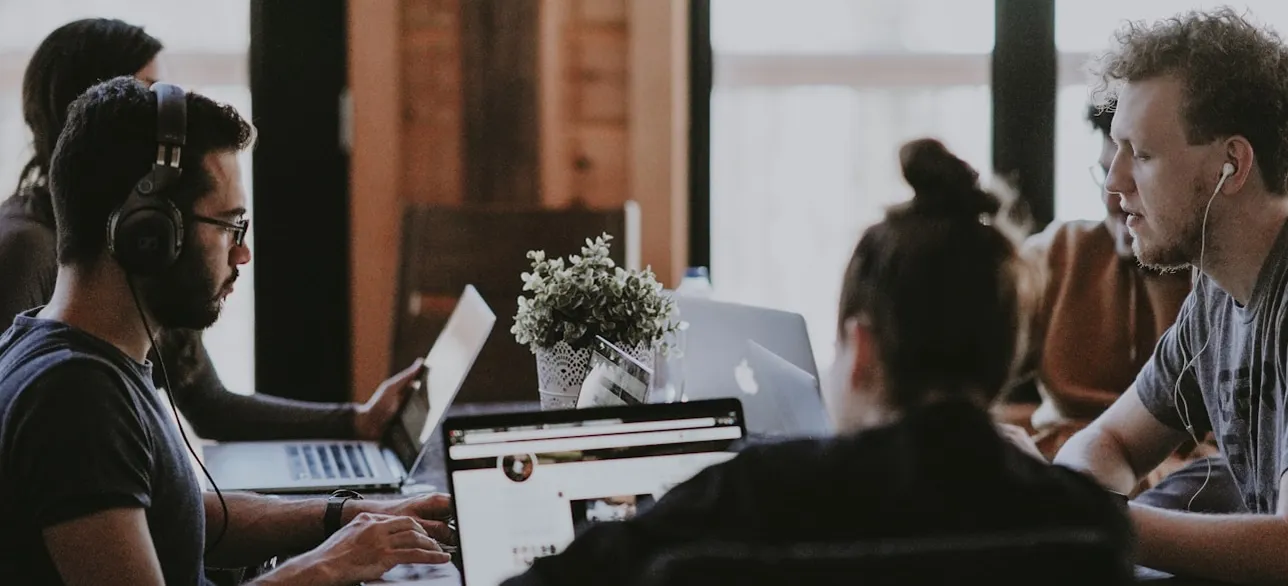 Group of people working on laptops in a shared space.