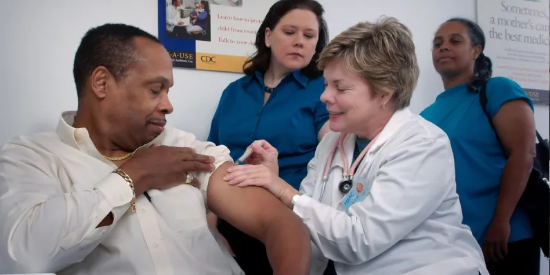 A healthcare worker administering a vaccine to a man while two other medical staff observe.